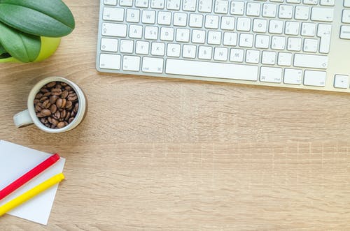 银色苹果魔术键盘在桌上的白色咖啡杯和咖啡豆 · 免费素材图片