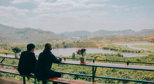 两人坐在湖和山前的椅子上 · 免费素材图片