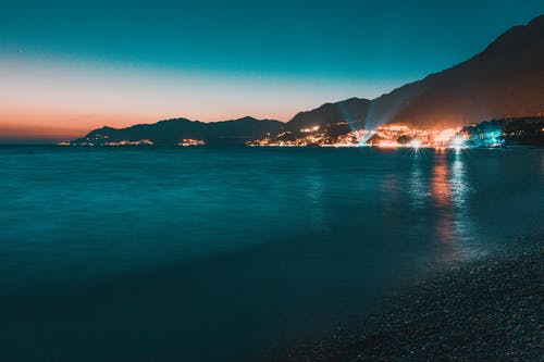 平静的水面，面对山附近的灯光城市 · 免费素材图片