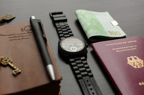 圆形黑色计时手表在德国护照附近的桌子上桌上的钞票 · 免费素材图片