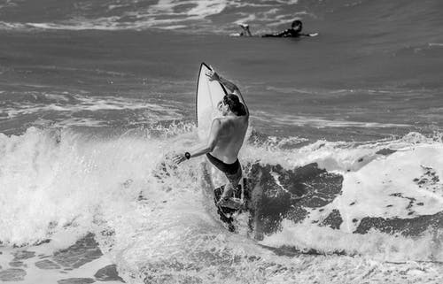 男子骑在海浪冲浪板上的灰度照片 · 免费素材图片