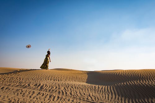 女人站在沙丘投掷帽子 · 免费素材图片