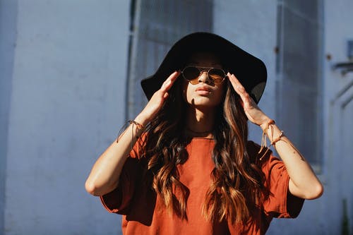 女人穿着白墙旁边的棕色衬衫和太阳帽 · 免费素材图片