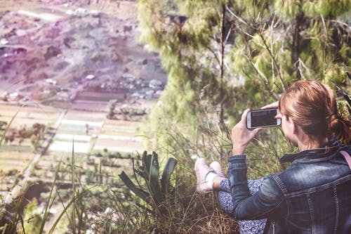 女人拿着智能手机，俯瞰平原 · 免费素材图片