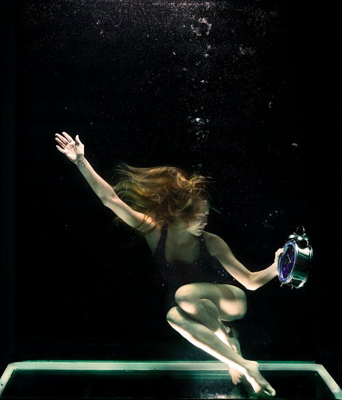 女人水下举行圆形灰色时钟 · 免费素材图片