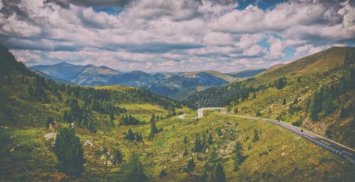 多云的蓝天下山间绿色松树包围的道路 · 免费素材图片