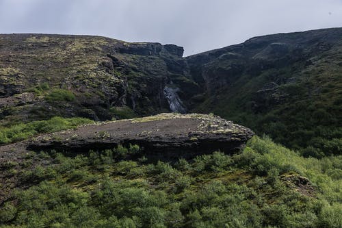 在白色的天空下山覆盖绿草的照片 · 免费素材图片