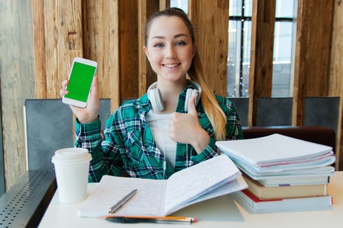 微笑的女人坐在桌前时，按住白色的android智能手机 · 免费素材图片