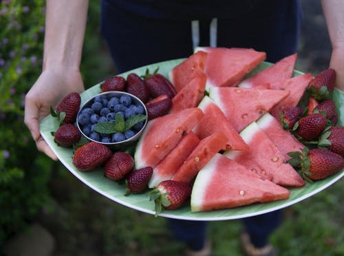 拿着椭圆形绿色盘子的人充满了切好的西瓜，草莓和蓝莓 · 免费素材图片
