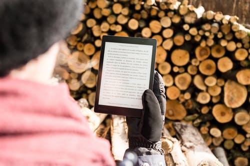 拿着黑电子书阅读器的人在堆木柴附近 · 免费素材图片