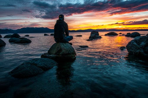 人坐在水体的岩石上 · 免费素材图片