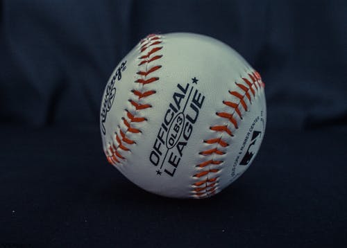 黑色纺织品上的白色和橙色官方职棒棒球 · 免费素材图片