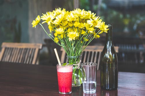 瓶子旁边的透明玻璃花瓶中的黄色雏菊 · 免费素材图片