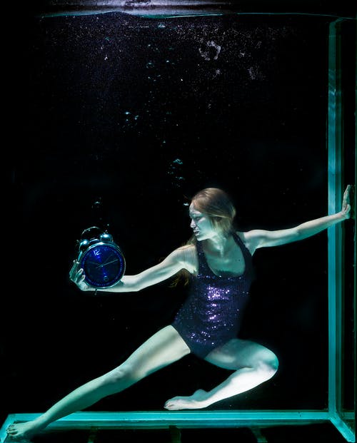 水下举行圆形蓝色模拟铃闹钟的女人 · 免费素材图片