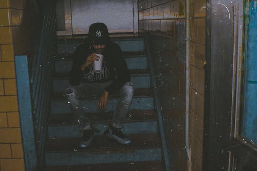 男子手持白色杯坐在楼梯上 · 免费素材图片