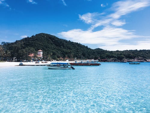 在小山旁边的水体上的两个白色和棕色小船 · 免费素材图片