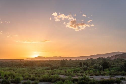日落期间被山包围的绿草田的航拍 · 免费素材图片