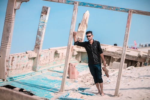 男子斜倚在木杆时拿着鞋 · 免费素材图片