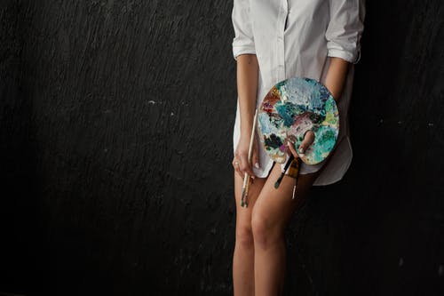 女人靠在黑色的表面，拿着油漆托盘和画笔 · 免费素材图片