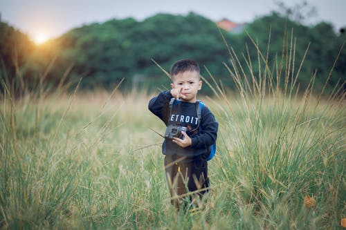 男孩站在绿色的田野，拿着黑色的相机 · 免费素材图片
