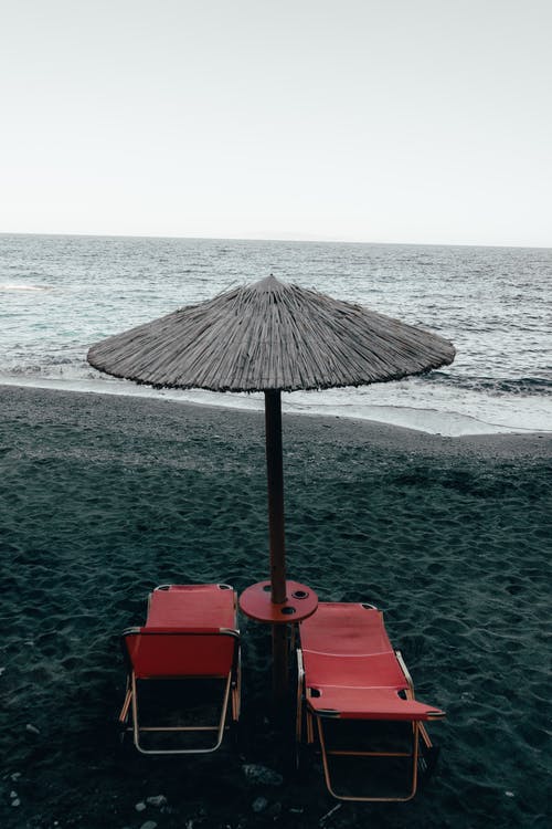 在岸边的露台伞下的两把红色泳池椅 · 免费素材图片