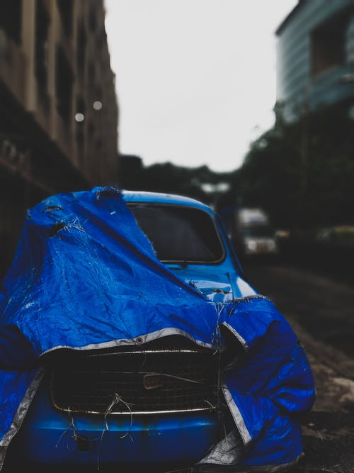 被遗弃的经典蓝色汽车与蓝色篷布停在混凝土建筑旁边 · 免费素材图片