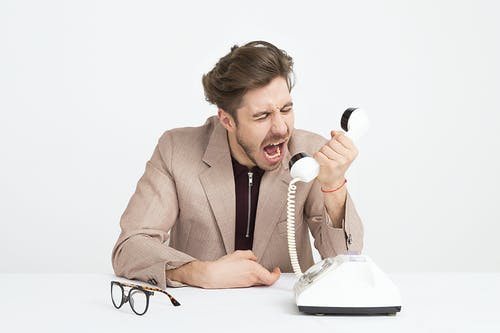 男人穿着棕色西装外套嘲笑白色电话 · 免费素材图片