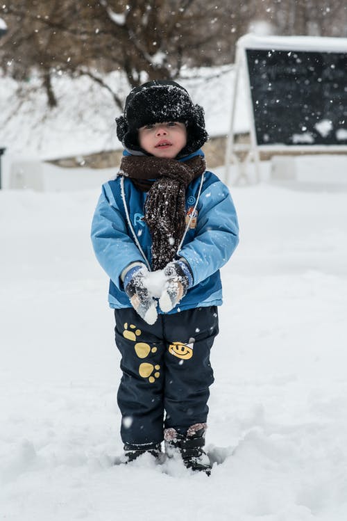 蹒跚学步站在雪地上抱着雪球 · 免费素材图片