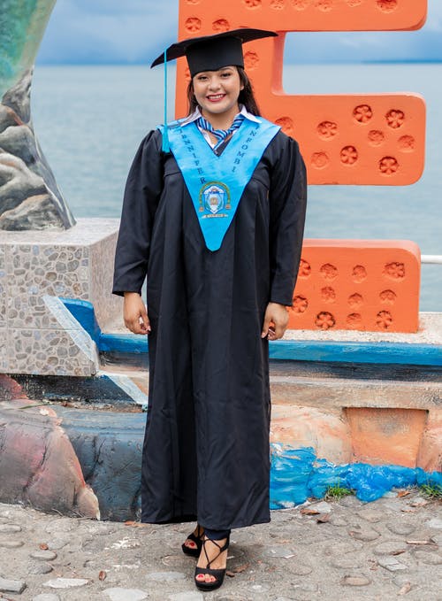 女人穿着橙色和蓝色字母e Standee的蓝色和黑色的学术礼服 · 免费素材图片