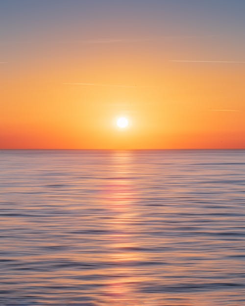 平静的水与太阳和橙色的天空 · 免费素材图片