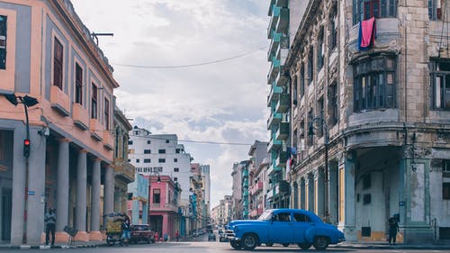 蓝色轿车在建筑物之间的道路上 · 免费素材图片