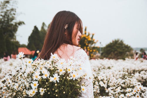 女人站在白色的雏菊花附近 · 免费素材图片