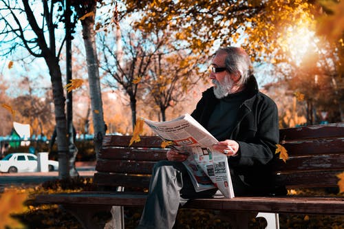 拿着报纸的人照片，当坐公园长椅时。 · 免费素材图片