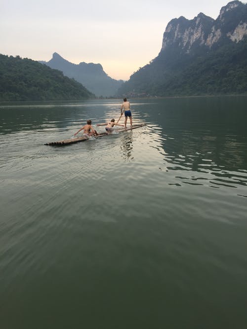 三个孩子在水上的棕色小船上 · 免费素材图片