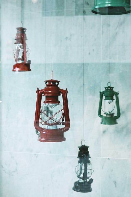 四个彩色金属气体灯笼挂在瓷砖墙附近 · 免费素材图片