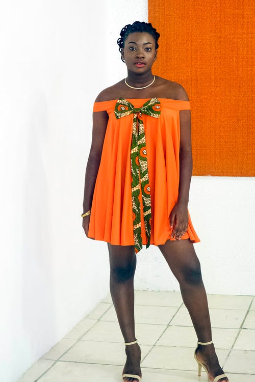穿橙色露肩礼服站在白墙上的女人的照片 · 免费素材图片