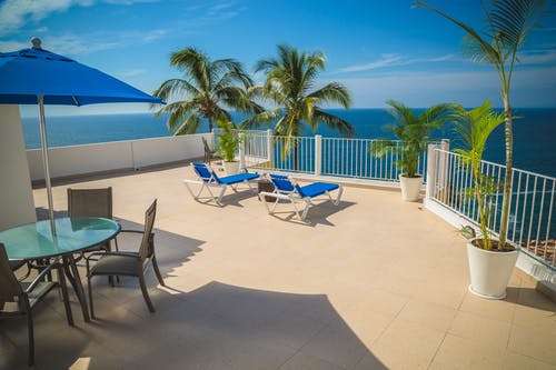 海洋景观摄影旁边的米色阳台上的蓝色躺椅 · 免费素材图片