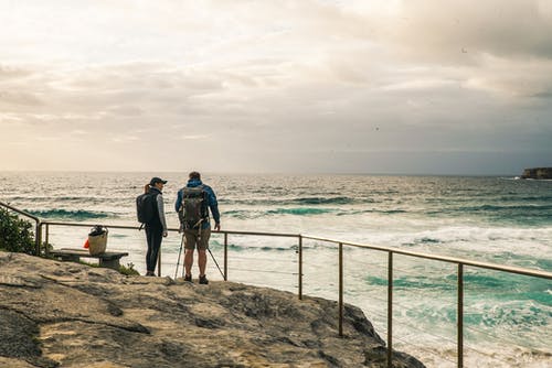 男人和女人站在岩石边与扶手在海洋旁边 · 免费素材图片