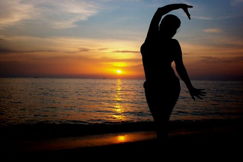 日落期间在海边上站立女人的剪影 · 免费素材图片