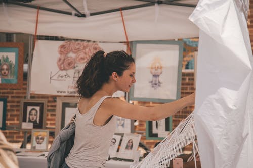 女人站在拿着白色的吊床的画旁 · 免费素材图片