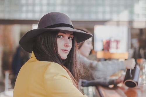 女人穿着灰色太阳帽和黄色的长袖上衣，回望房间 · 免费素材图片