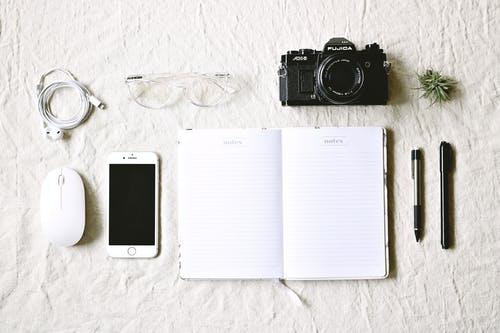 笔和金色iphone 6和相机旁边的白色笔记本 · 免费素材图片