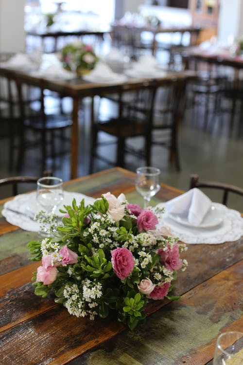 酒杯和盘子在棕色的桌子旁边的粉红色和白色的花焦点 · 免费素材图片