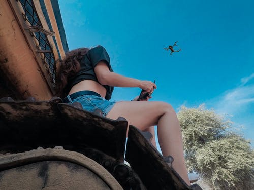 女人坐在屋顶上使用黑色quadcopter无人机 · 免费素材图片