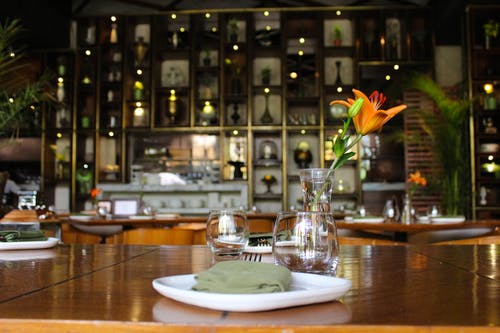 橙色黄花菜在透明玻璃投手上棕色木制餐桌与餐具 · 免费素材图片