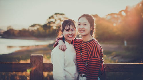 两个女人站在棕色的篱笆旁边 · 免费素材图片