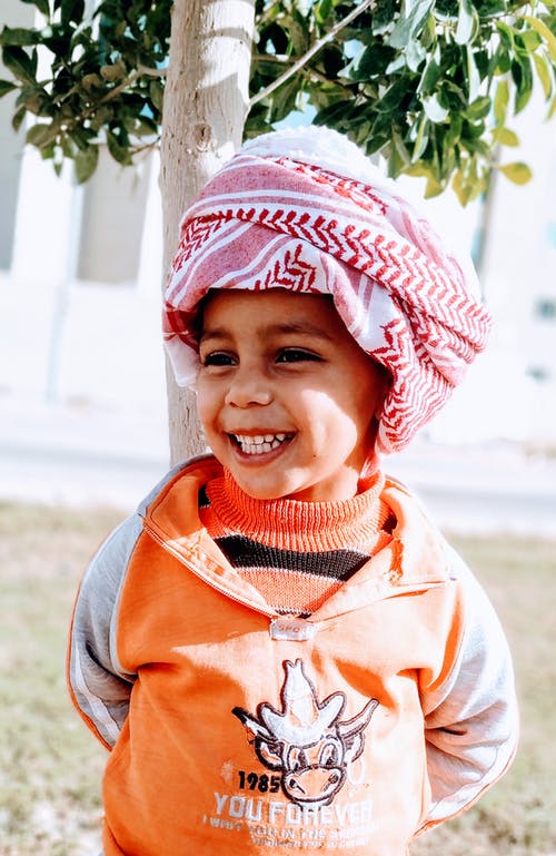 微笑的男孩，在keffiyeh站在附近的树的照片 · 免费素材图片