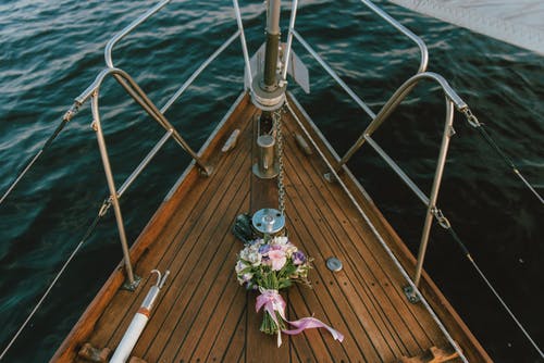 在水面上的棕色木制船上的白色和紫色花朵花束 · 免费素材图片