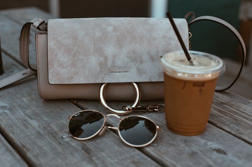 饮料和太阳镜旁边的皮革斜挎包 · 免费素材图片