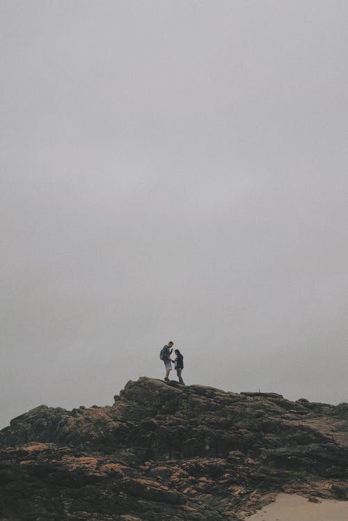 男人和女人站在白色的天空下的岩石上 · 免费素材图片